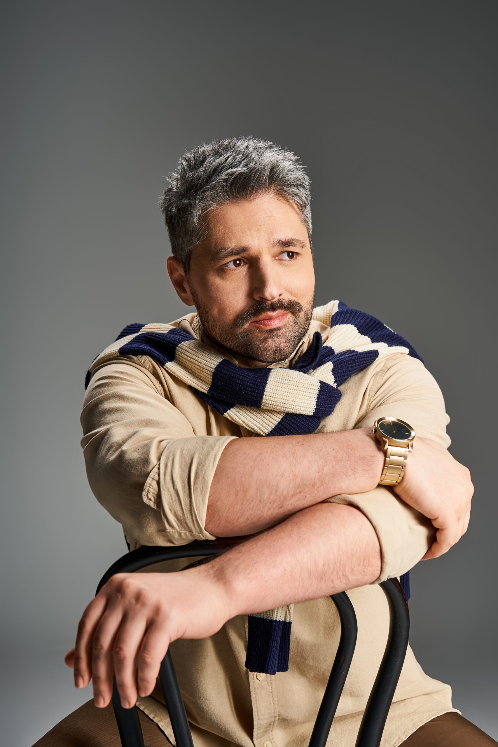 Handsome man with a stylish outfit poses confidently against a neutral backdrop.